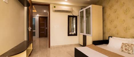 Une chambre d’hôtel comprenant un lit, une armoire, un miroir, un appareil de climatisation et une porte donnant sur une autre pièce.