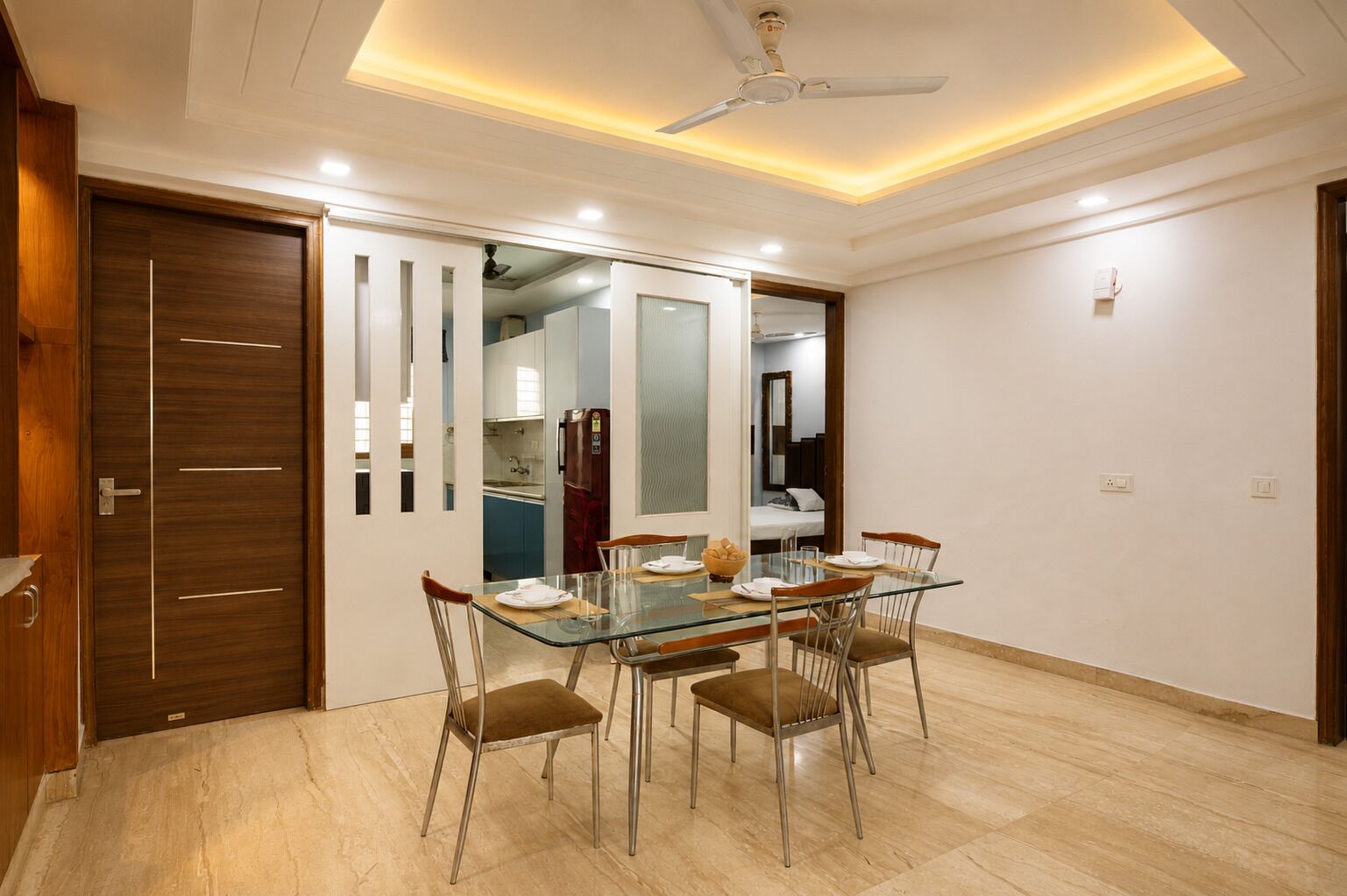 A dining area with a glass table, metal chairs, a ceiling fan, and a wooden door.