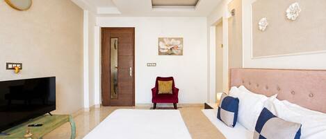 A hotel room with a bed, a TV, a red chair, a ceiling fan, and a painting on the wall.