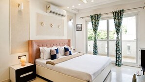 Ein Schlafzimmer mit einem Bett, Nachttisch, wandmontierter Klimaanlage, Deckenventilator und großen Fenstern mit Vorhängen.