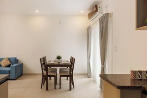 A dining area with a table, chairs, a blue sofa, and a kitchen counter. - Aero Rosewood by Red Olive 3bhk 5min Airport (Bengaluru)