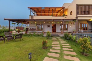 A two-story house with a covered patio, outdoor seating, and a stone pathway leading to the entrance.