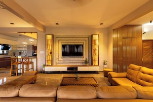 Una sala de estar moderna con un televisor de pantalla plana grande, sofás de cuero, una mesa de centro y una cocina al fondo.