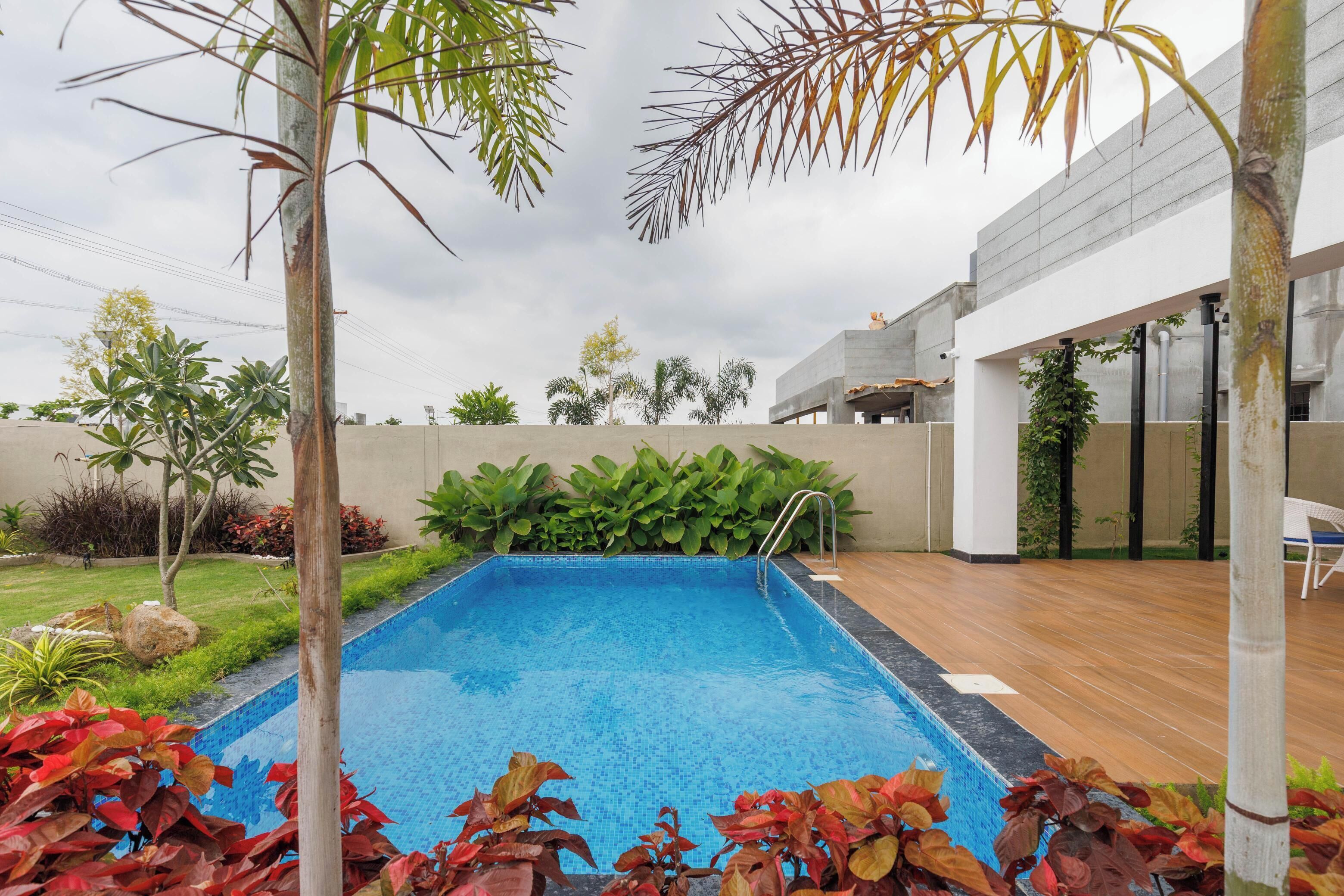 A swimming pool with a wooden deck, surrounded by plants and a modern building.