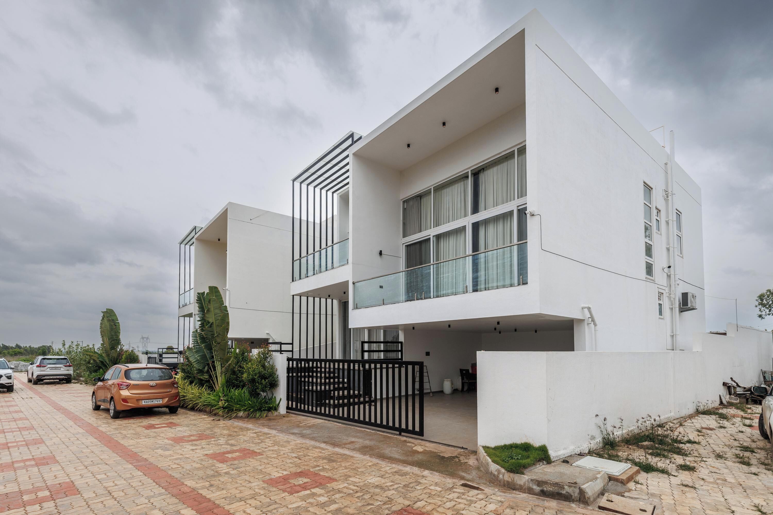 A modern two-story residential building with a flat roof, large windows, and a covered driveway.