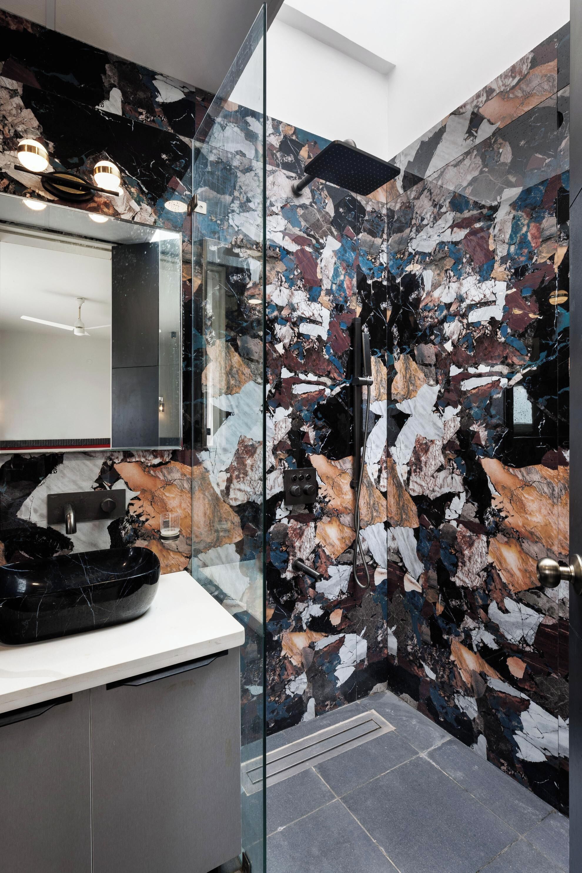 A modern bathroom with a glass shower enclosure, a white countertop, and a marble backsplash.