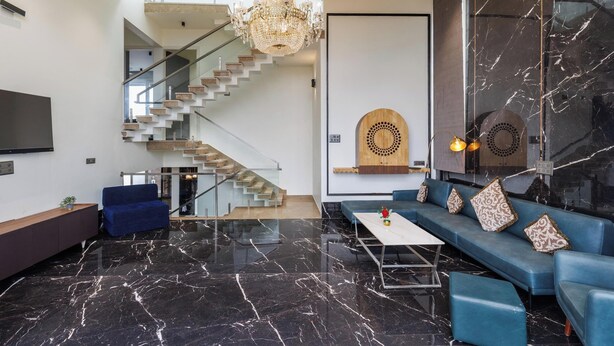 A modern living room with a marble floor, a staircase, a chandelier, a blue sofa set, and a large wall-mounted TV.