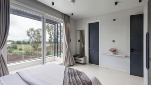 A bedroom with a large window, a bed, a dresser, a mirror, and a door.