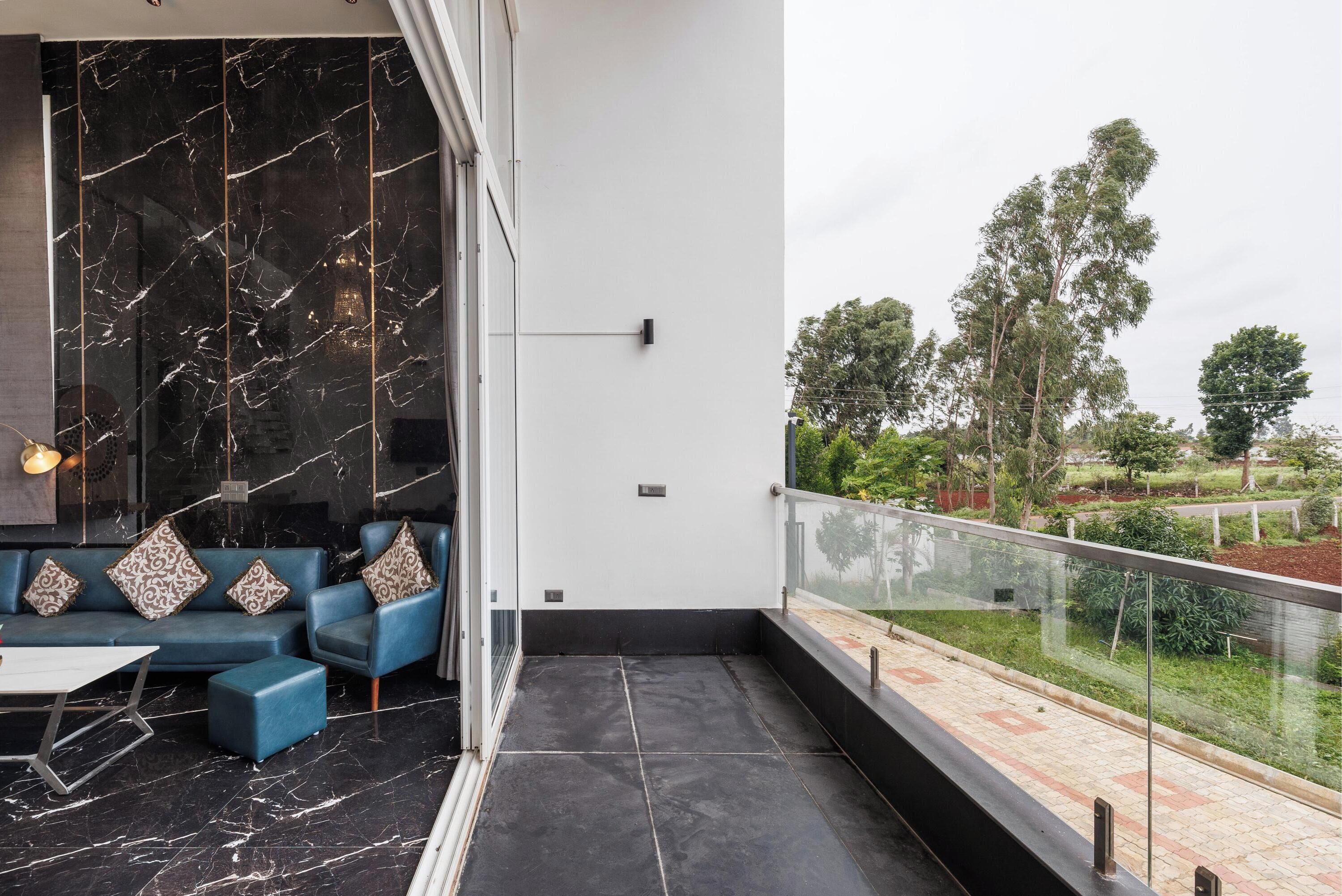 Un salon moderne avec un canapé bleu, un mur en marbre et un balcon doté d’une balustrade en verre donnant sur un espace verdoyant.
