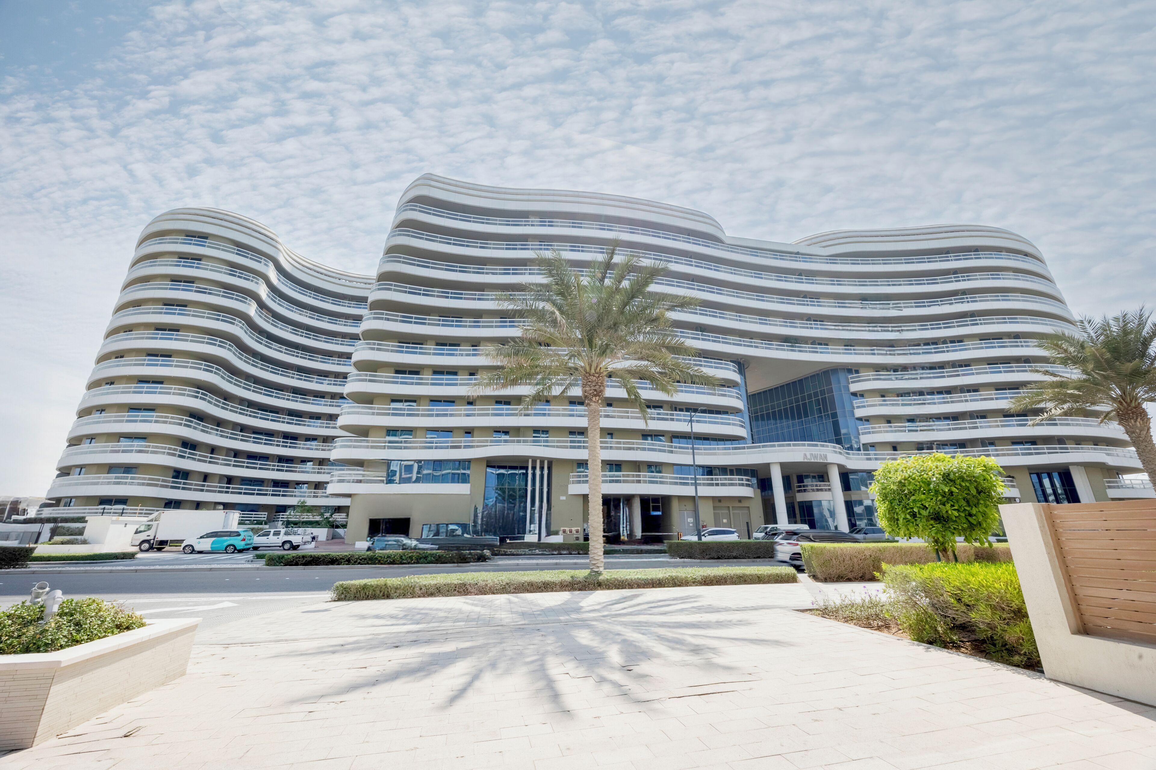 Un hotel moderno con fachada curva, varios balcones y un área de entrada ajardinada.