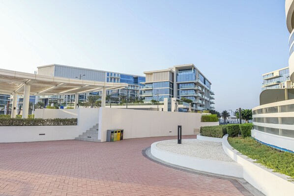 Un edificio moderno con una galería techada, un área ajardinada con jardín circular y una escalera que conduce a un nivel superior.