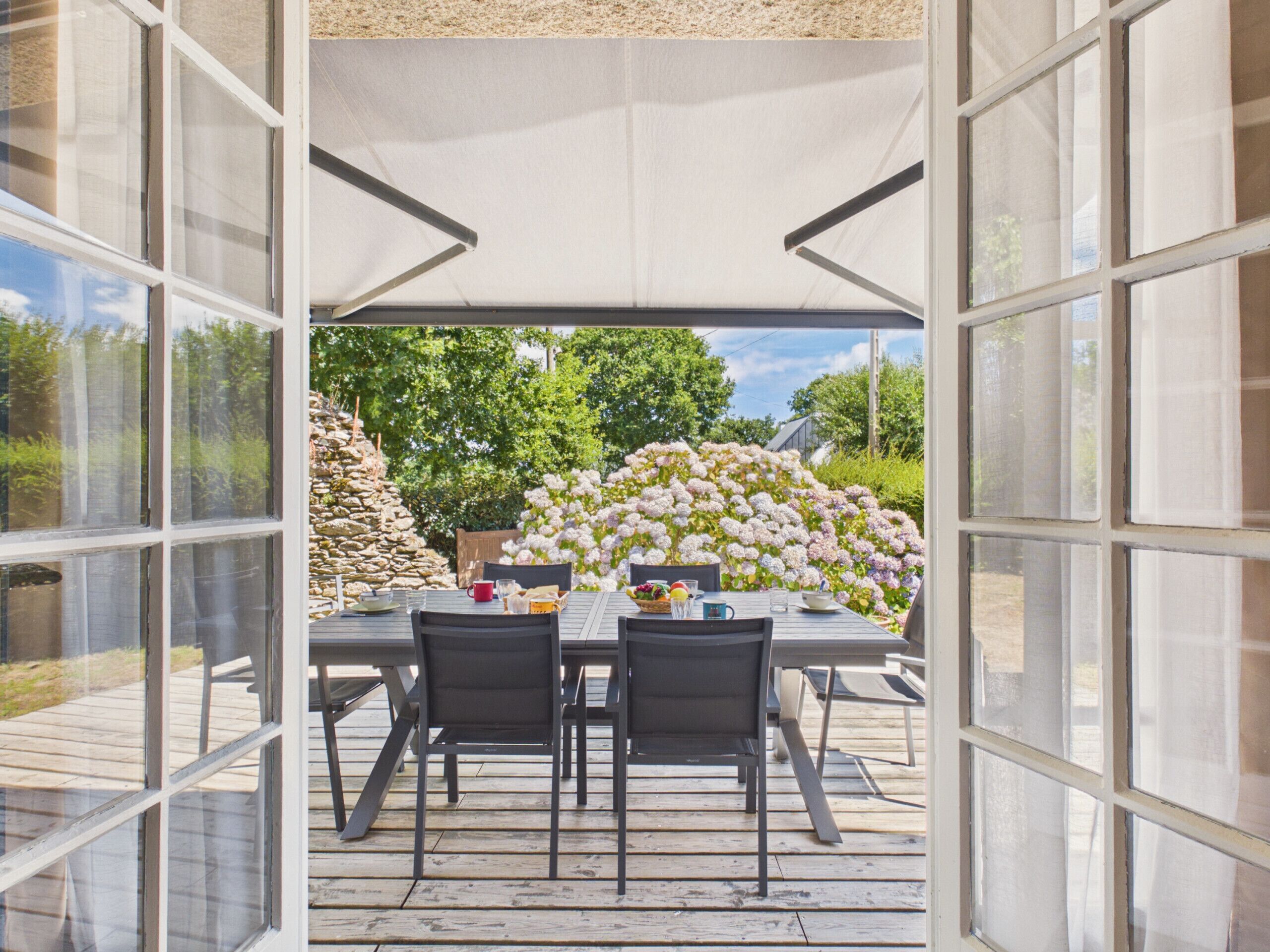 An outdoor patio with a table and chairs, surrounded by a garden with flowering plants.
