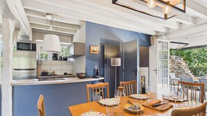 A modern kitchen with a central island, dining table with chairs, and a view of the outdoors. - Stone house for 5, garden, beach 700m away (Sarzeau)