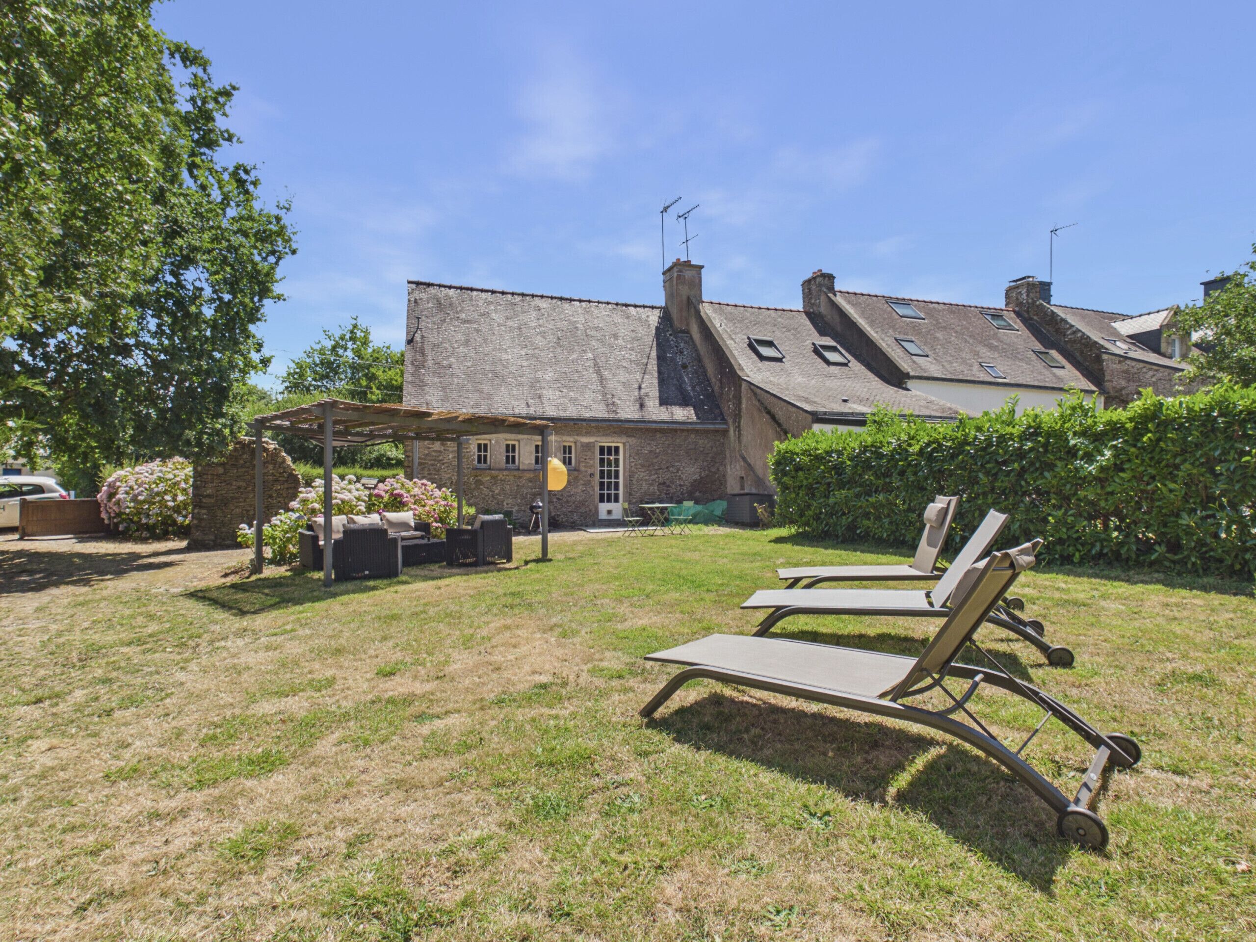 A stone building with a sloped roof, a covered patio with outdoor furniture, and a grassy lawn.