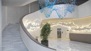 A curved marble staircase leading to a lobby with a modern design, including a large potted plant and a unique ceiling light fixture.