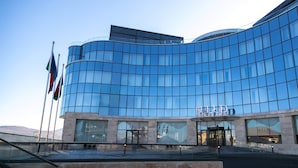 A modern building with a curved glass facade, a prominent entrance with glass doors, and flags on the left.