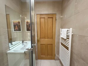 A bathroom with a wooden door, a white sink, a mirror, and a towel rack. - Charming Edinburgh Stay Near the Shore (Edinburgh)
