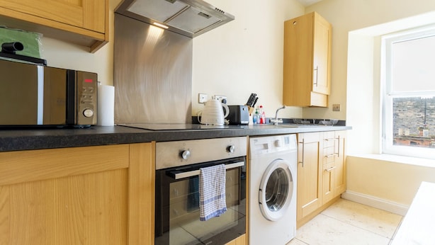 A modern kitchen with stainless steel appliances, wooden cabinets, and a view of the city through a window. - Charming Edinburgh Stay Near the Shore (Edinburgh)