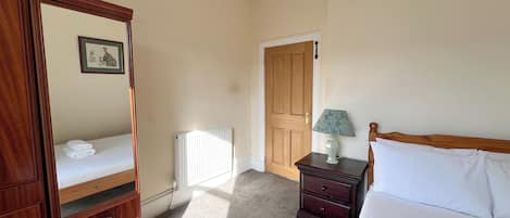 A bedroom with a wooden dresser, a bedside table with a lamp, a radiator, and a door.
