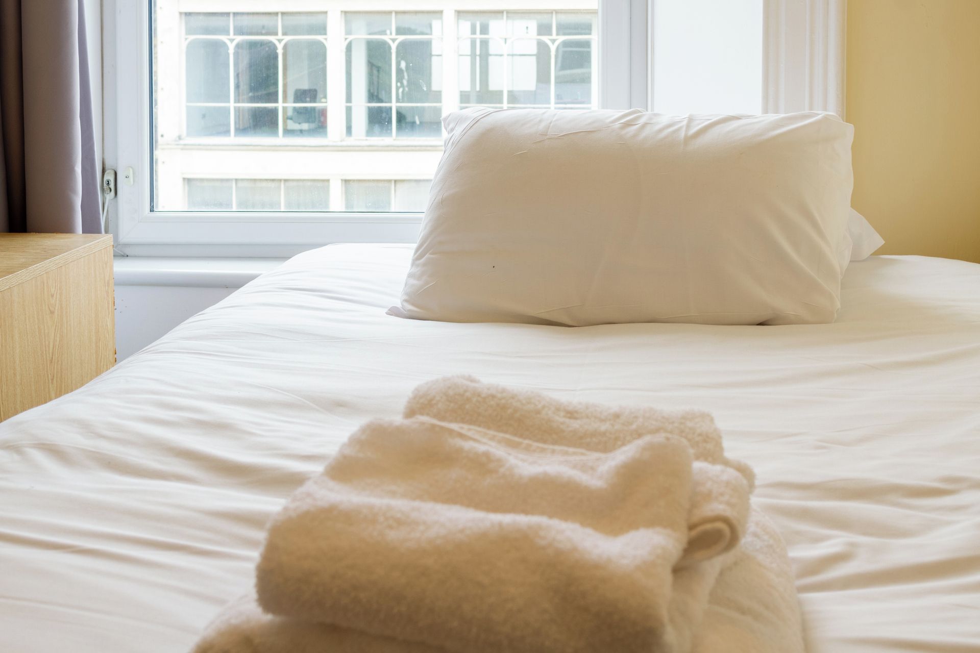 Een net opgemaakt bed met een wit kussen en een opgevouwen deken.