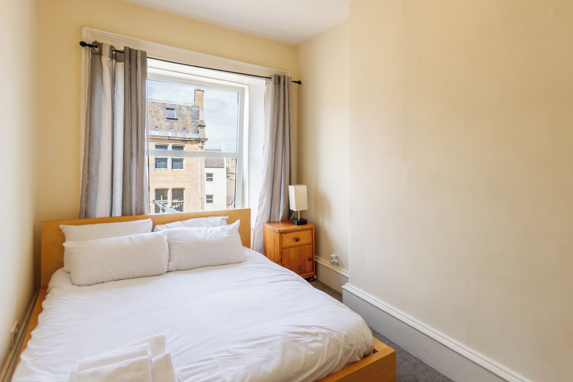 A hotel room with a bed, a nightstand, a lamp, and a window with curtains.