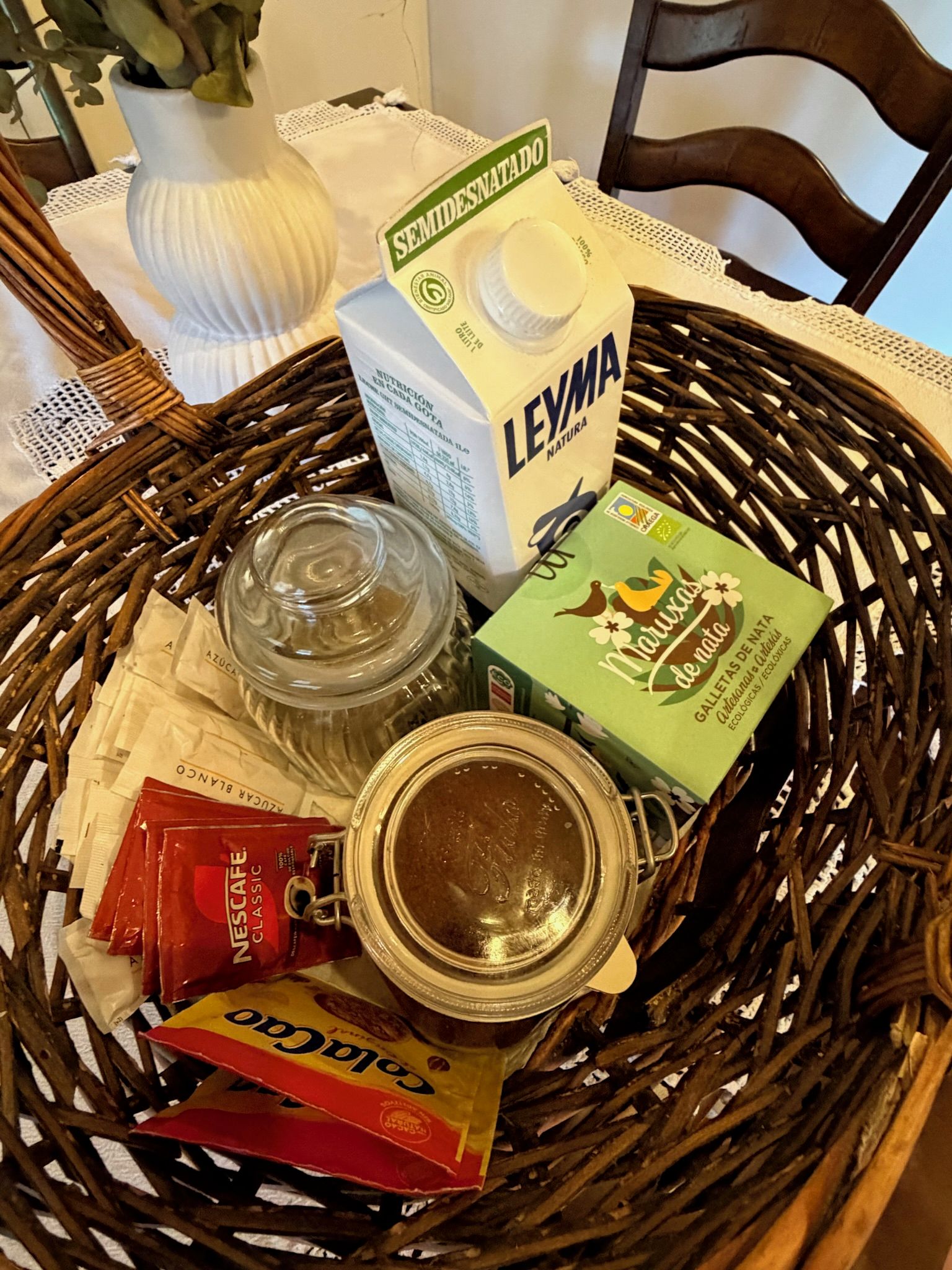 Un panier en osier contenant un carton de lait « semidesnatado », un bocal, une boîte de « Maruxas de nata » et un paquet de café « Nescafe Classic ».