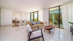 Un salon moderne comprenant un canapé, un fauteuil et une table basse, un coin repas avec des chaises, et de grandes fenêtres avec des rideaux.