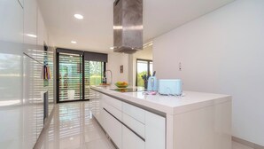 Une cuisine moderne dotée d’un grand îlot central, de meubles aux lignes épurées et offrant une vue à travers la porte vitrée.
