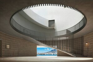 A modern interior with a spiral staircase, a view of a harbor, and a brick wall. - The Cape Town EDITION (CAPE TOWN)
