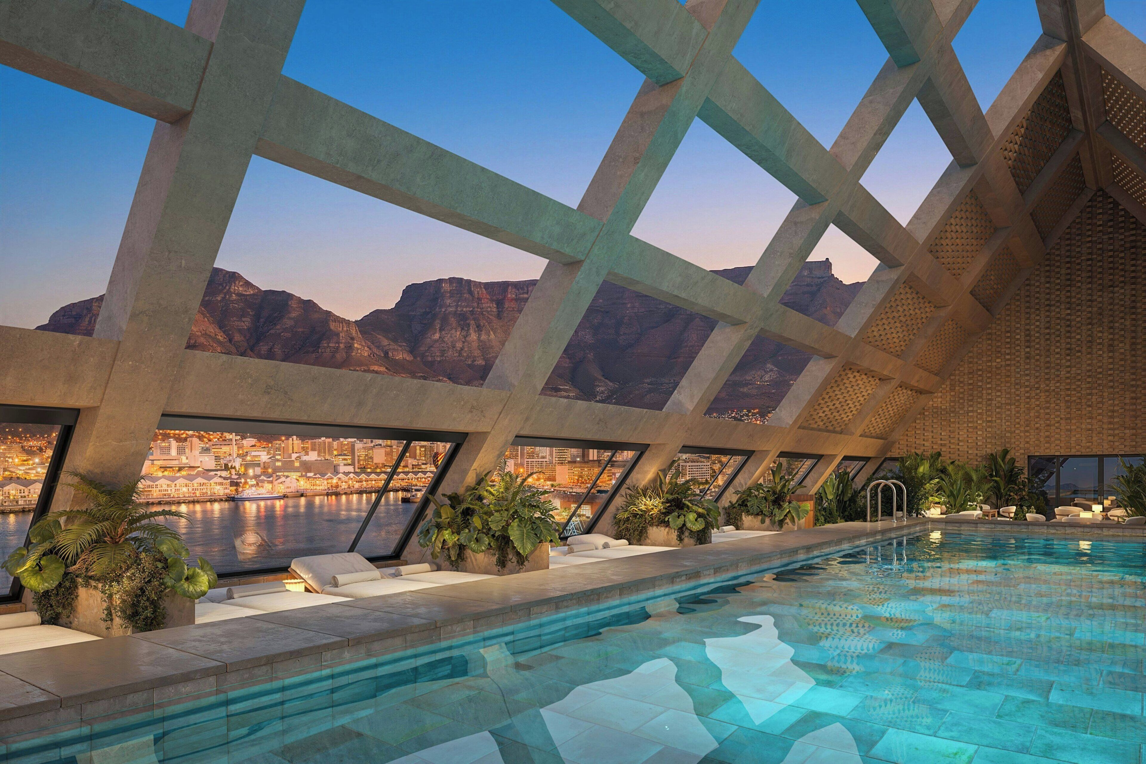 An indoor swimming pool with a cityscape view through a geometric ceiling structure.