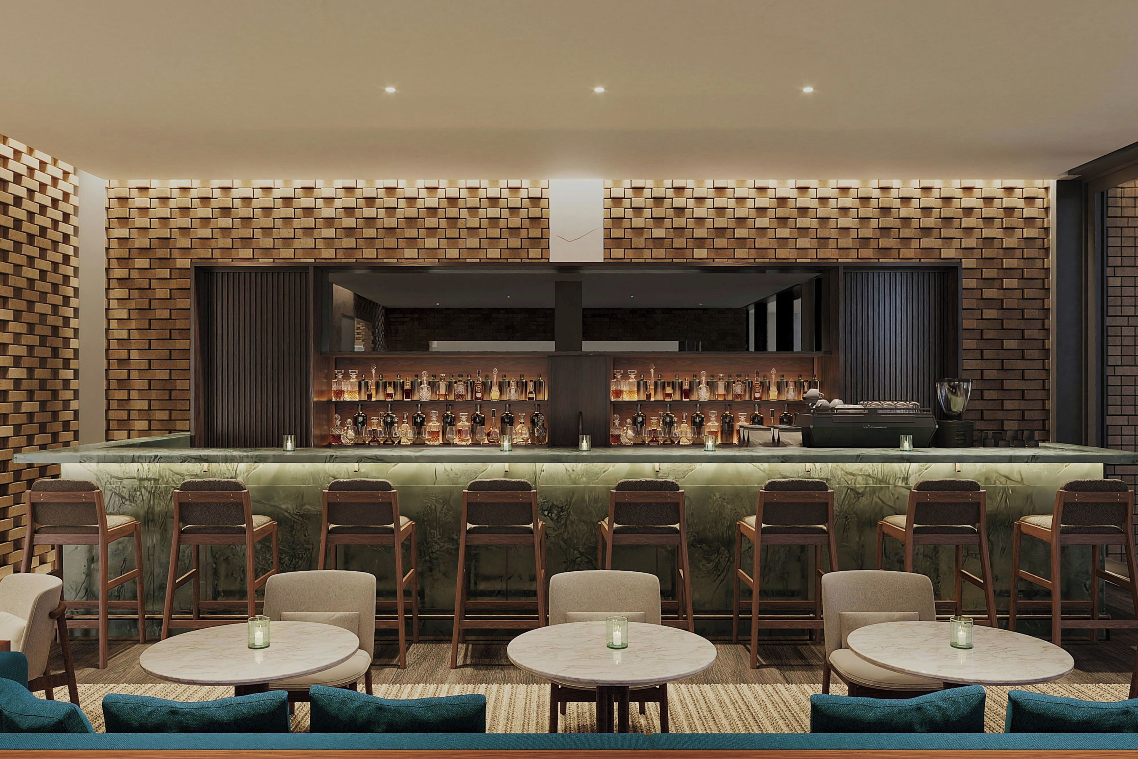 Zona de bar con pared de ladrillo, varias mesas y sillas, y una variedad de botellas en estanterías.