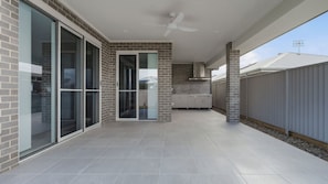 Ein überdachter Patio-Bereich mit einer Schiebetür, einem Deckenventilator und einer Küchenzeile mit Schränken.