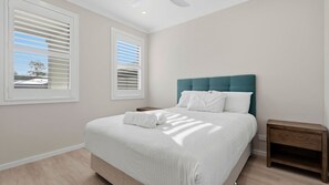 Ein Schlafzimmer mit einem Bett, zwei Fenstern mit Jalousien, einem Nachttisch und einem Deckenventilator.