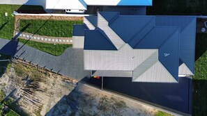 Een luchtbeeld van een modern gebouw met een opvallend geometrisch dak, omgeven door een verzorgd gazon en een verharde oprit.