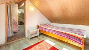Ein Schlafzimmer mit schrägen Wänden, einem Bett mit farbenfroher Streifenoptik, einem kleinen weißen Nachttisch und einem roten Teppich.