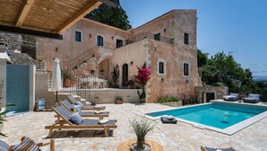 A poolside area with lounge chairs, a small table, and a stone building with a staircase. - 3-bed Armeni Mountain Oasis (Rethymno)