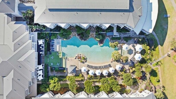 Vue aérienne d’un complexe hôtelier comprenant une piscine, des espaces de détente et plusieurs bâtiments.