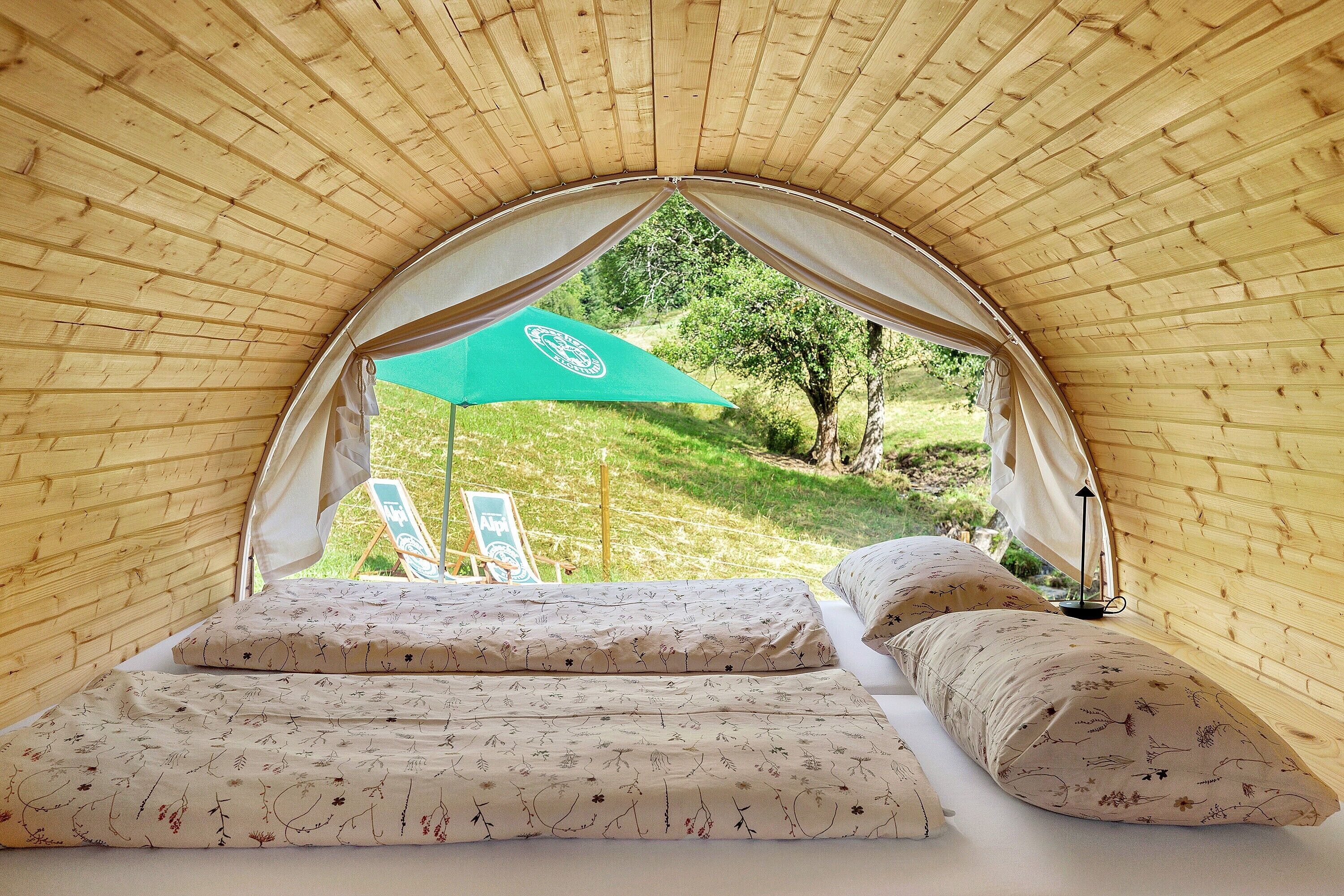 A tent with a bed, pillows, and a green umbrella.