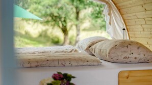 Een tent met een bed, kussens en uitzicht op groen.