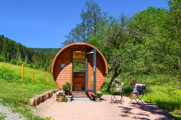 Una cabaña de madera con diseño circular, una puerta y una pequeña mesa con una silla afuera.