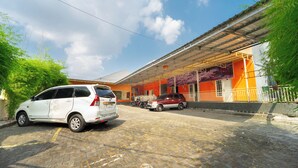 A building with a covered entrance, parked cars, and a paved area. - Sunrise 888 By ARBA (Semarang)