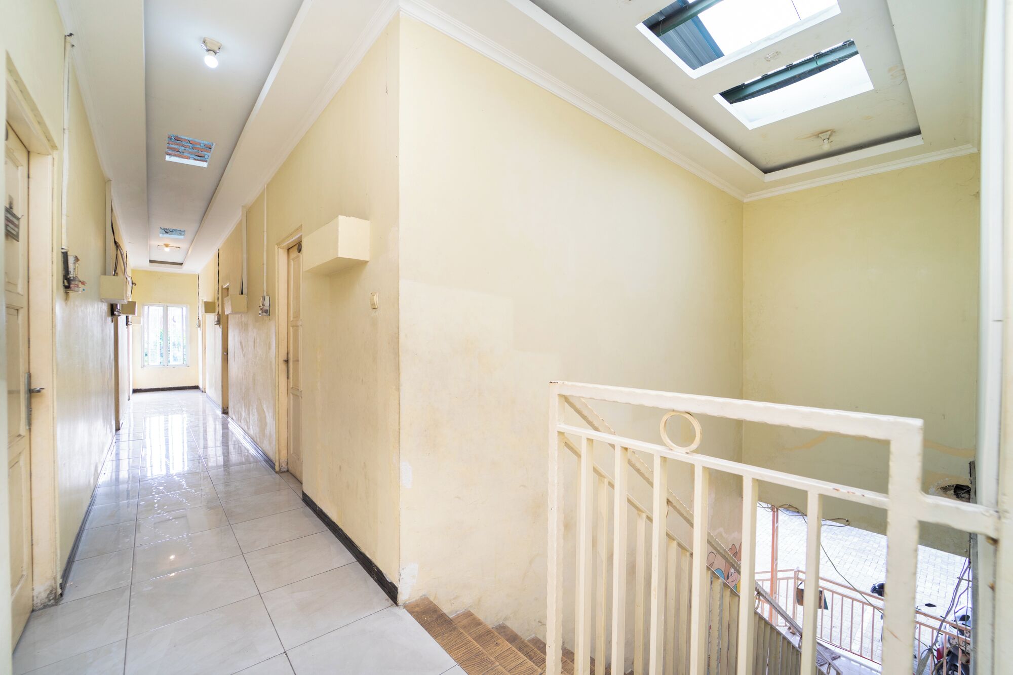 A corridor with a tiled floor, a white railing, and a skylight.