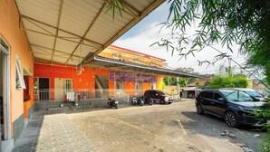 A building with a covered entrance, a paved area, and parked vehicles. - Sunrise 888 By ARBA (Semarang)