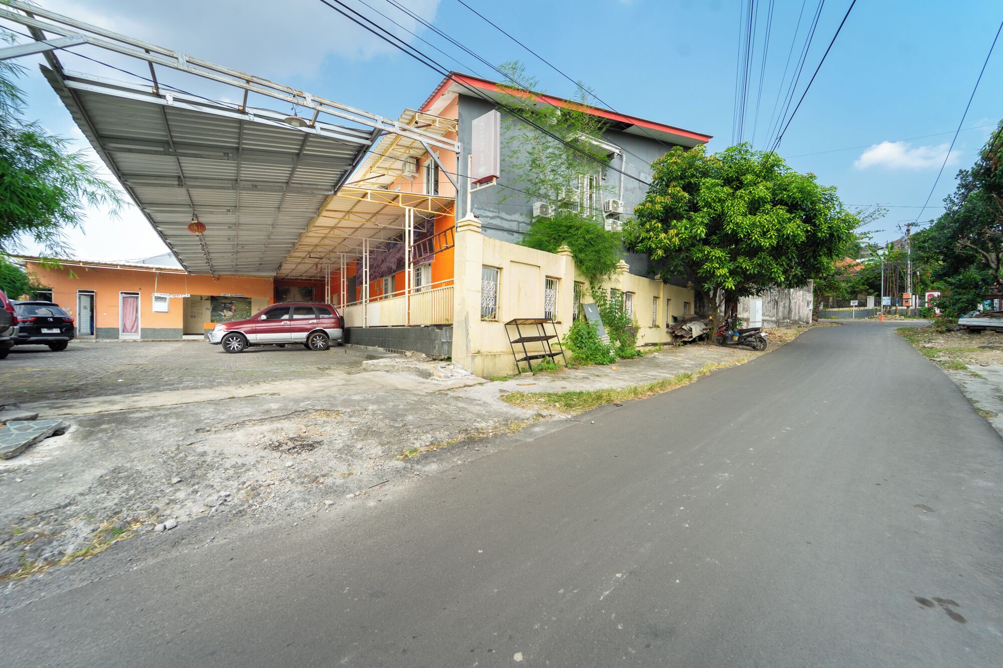 A street with a parked car, a building with a red roof, and a covered area with a metal roof.