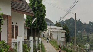 A rural road with houses on either side, a motorcyclist in the distance, and power lines overhead. - Cozzy Villa Pangi (Bandung)