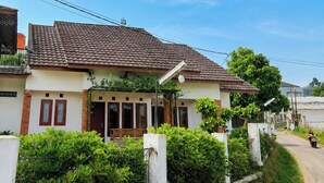 A two-story house with a tiled roof, a porch with a bench, and a street view. - Cozzy Villa Pangi (Bandung)
