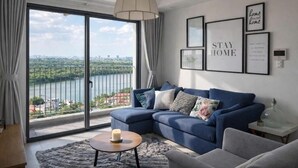 Un salon moderne avec un canapé d’angle bleu, une table basse ronde et une vue sur une rivière et le paysage urbain, gr âce à de grandes portes coulissantes.