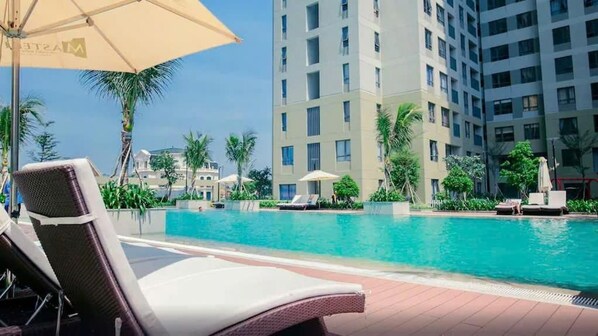 A poolside area with lounge chairs, umbrellas, and a tall building in the background. - Masteri Thao Dien Apartment Raymond Holm (An Khanh)