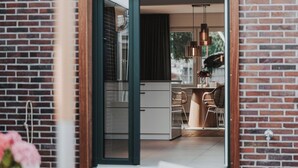 Eine moderne Küche mit einem großen Fenster, einem Essbereich mit weißen Stühlen und einer Außenwand aus Ziegelsteinen.