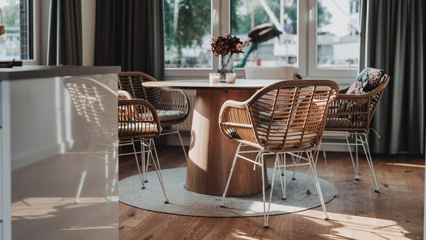 Ein moderner Essbereich mit Korbstühlen, einem runden Holztisch und einer Vase mit Blumen.